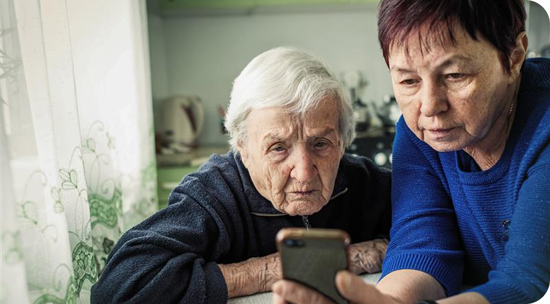 Representación actoral de una mujer anciana y su cuidadora mirando la pantalla de un teléfono, discutiendo la agitación que puede ocurrir con la demencia debido a la enfermedad de Alzheimer.