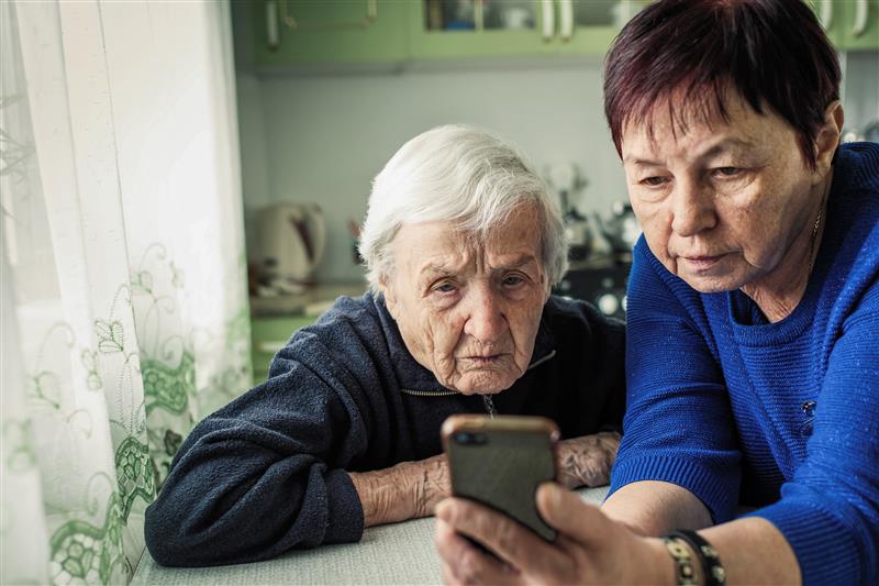 Representación actoral de una mujer anciana y su cuidadora mirando la pantalla de un teléfono, discutiendo la agitación que puede ocurrir con la demencia debido a la enfermedad de Alzheimer.