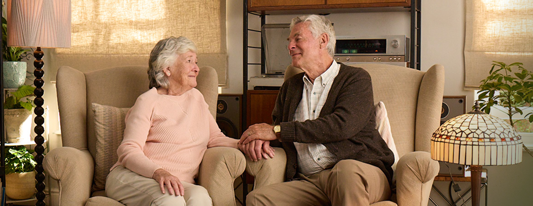 Actor portrayal of elderly man holding hands and smiling with his wife with agitation that may happen with dementia due to Alzheimer's disease.