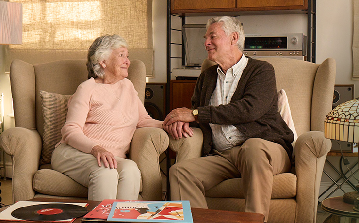 Actor portrayal of elderly man holding hands and smiling with his wife with agitation that may happen with dementia due to Alzheimer's disease.