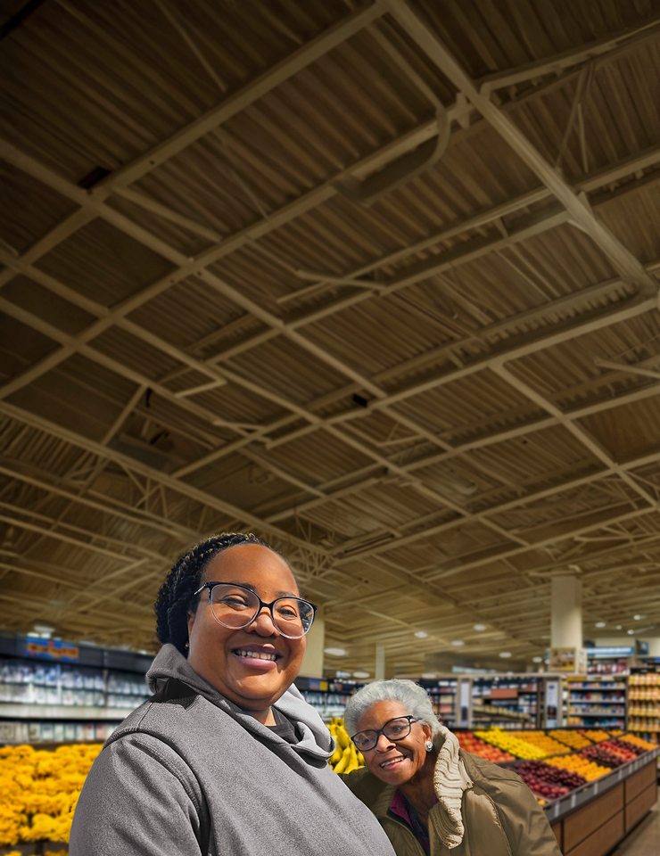 Caregiver Natasha and her grandmother with agitation that may happen with dementia due to Alzheimer's disease hugging and smiling in supermarket aisle.