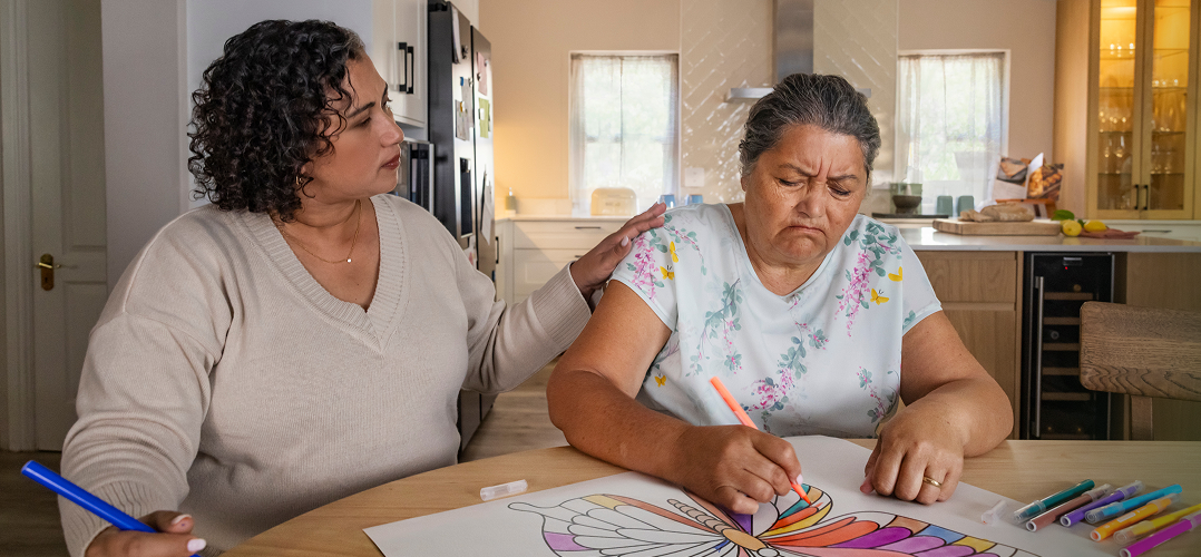 Actor portrayal of adult daughter comforting elderly mother coloring an image of a butterlfy who's living with agitation that may happen with dementia due to Alzheimer's disease.