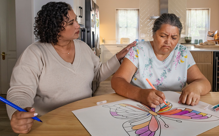 Actor portrayal of adult daughter comforting elderly mother coloring an image of a butterlfy who's living with agitation that may happen with dementia due to Alzheimer's disease.